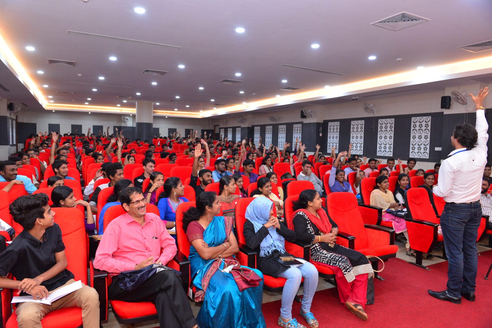 Santosh Talaghatti engaging hundreds of students in an interactive auditorium session with hands raised
